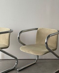 two chairs with chrome legs and beige suede